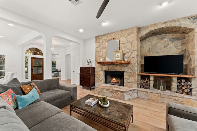 living room with wood-type flooring, a stone fireplace, and ceiling fan