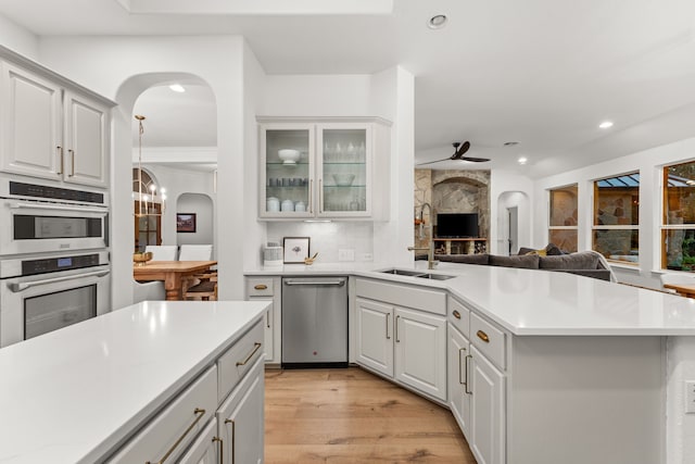 kitchen with sink, light hardwood / wood-style flooring, stainless steel appliances, white cabinets, and ceiling fan with notable chandelier