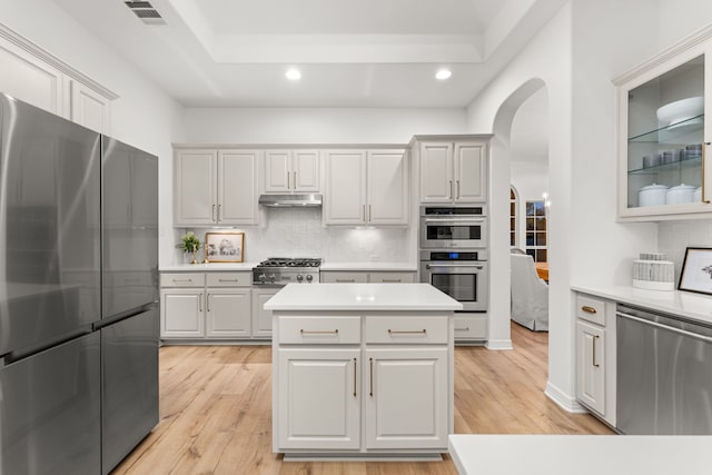 kitchen with tasteful backsplash, white cabinets, a center island, stainless steel appliances, and light wood-type flooring