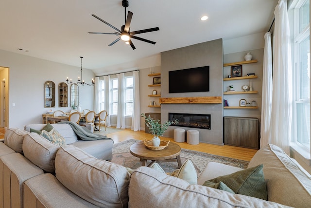 living room with light hardwood / wood-style flooring, a large fireplace, radiator, built in features, and ceiling fan with notable chandelier