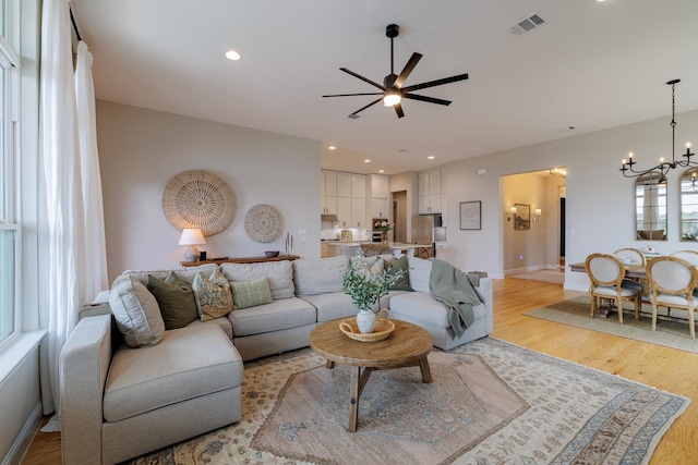 living room featuring ceiling fan with notable chandelier and light hardwood / wood-style flooring