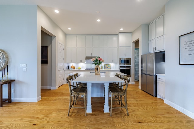 kitchen with white cabinetry, a kitchen breakfast bar, decorative backsplash, a large island, and stainless steel appliances