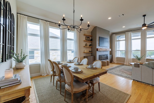 dining room with ceiling fan with notable chandelier, a large fireplace, a healthy amount of sunlight, and light wood-type flooring