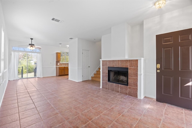 unfurnished living room with a tile fireplace, ceiling fan, and light tile patterned flooring