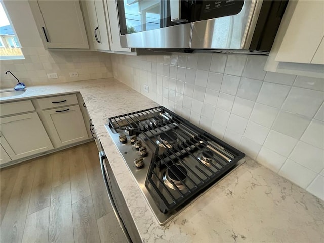 kitchen featuring sink, light hardwood / wood-style flooring, stainless steel appliances, light stone counters, and tasteful backsplash