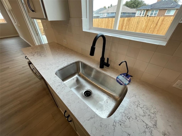 interior details with wood-type flooring, sink, backsplash, and light stone counters