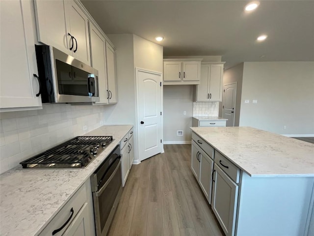 kitchen with light stone counters, a kitchen island, stainless steel appliances, light hardwood / wood-style floors, and backsplash