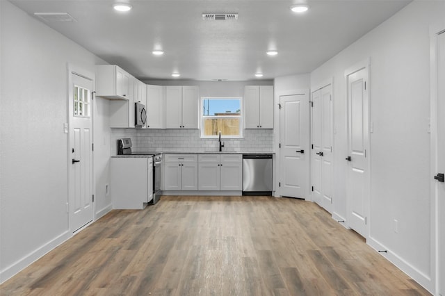 kitchen featuring hardwood / wood-style floors, sink, white cabinets, backsplash, and stainless steel appliances