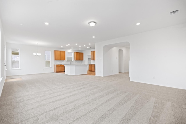 unfurnished living room featuring light carpet and a notable chandelier