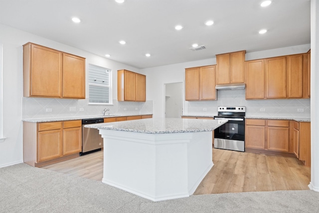 kitchen featuring light stone counters, light hardwood / wood-style flooring, appliances with stainless steel finishes, a kitchen island, and backsplash