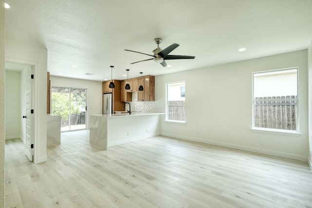 unfurnished living room with ceiling fan, sink, a textured ceiling, and light wood-type flooring