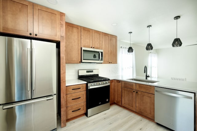 kitchen with pendant lighting, sink, stainless steel appliances, tasteful backsplash, and light wood-type flooring