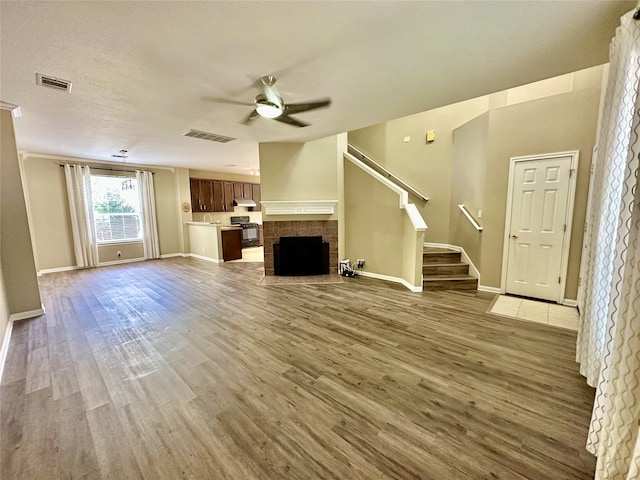 unfurnished living room featuring wood-type flooring, a tile fireplace, and ceiling fan