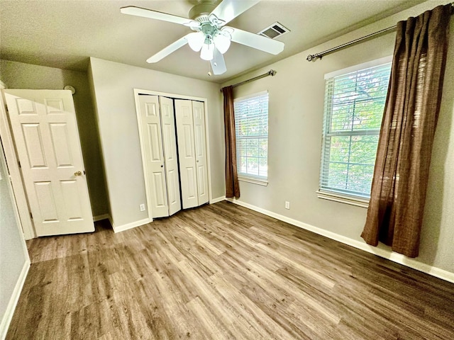 unfurnished bedroom featuring multiple windows, light hardwood / wood-style flooring, a closet, and ceiling fan