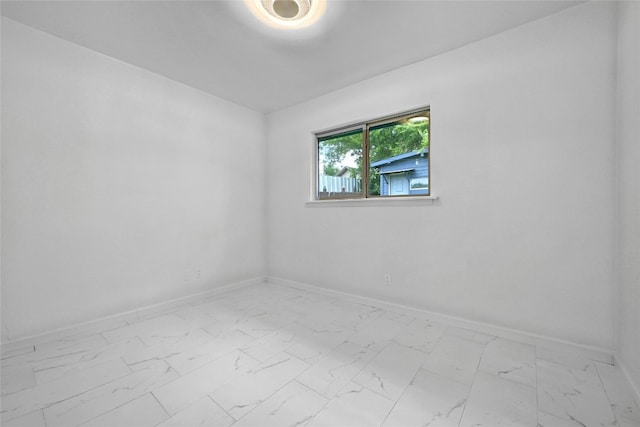 spare room featuring marble finish floor and baseboards