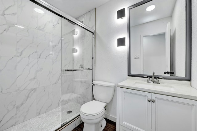 bathroom featuring a marble finish shower, a textured wall, vanity, and toilet