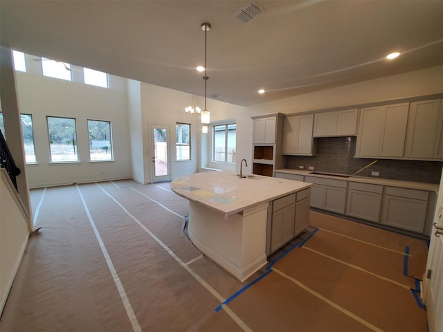 kitchen with sink, a kitchen island with sink, backsplash, black electric cooktop, and decorative light fixtures