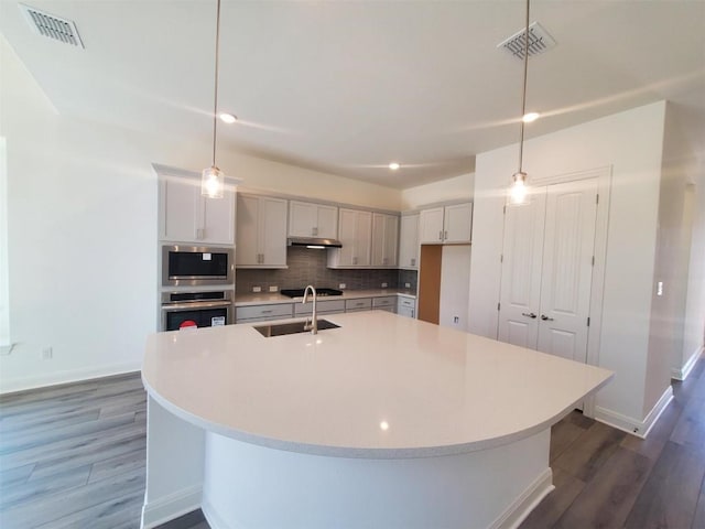 kitchen with visible vents, hanging light fixtures, appliances with stainless steel finishes, light countertops, and a center island with sink