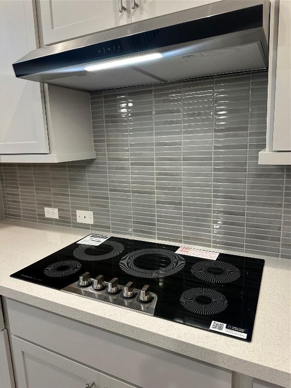 interior details with white cabinetry, light countertops, under cabinet range hood, and black electric cooktop