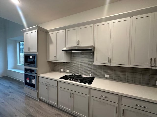 kitchen with light countertops, stainless steel oven, built in microwave, under cabinet range hood, and black electric cooktop