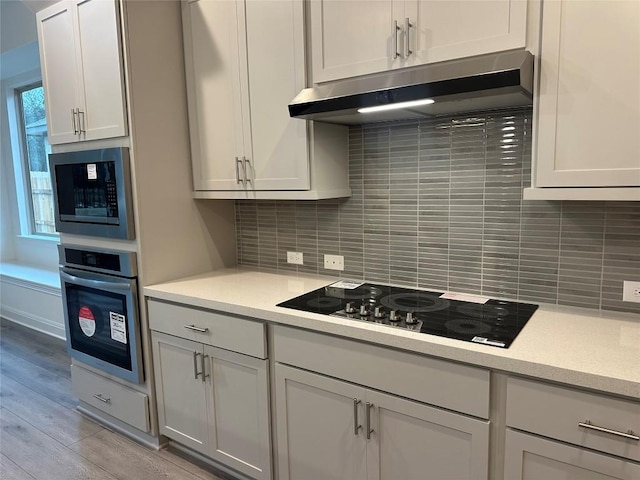 kitchen featuring under cabinet range hood, stainless steel appliances, white cabinets, light countertops, and tasteful backsplash