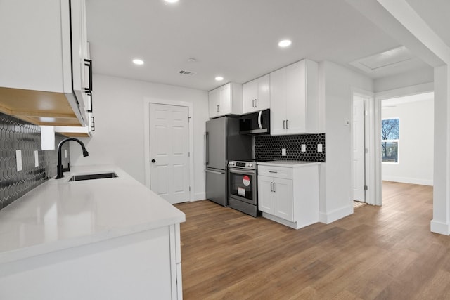 kitchen featuring sink, appliances with stainless steel finishes, white cabinetry, decorative backsplash, and light wood-type flooring