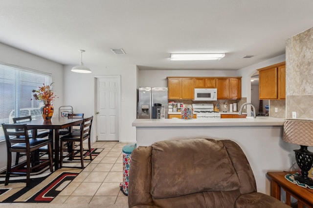 kitchen featuring light tile patterned floors, white appliances, hanging light fixtures, backsplash, and kitchen peninsula