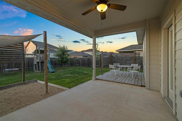 patio terrace at dusk with a playground, ceiling fan, and a lawn