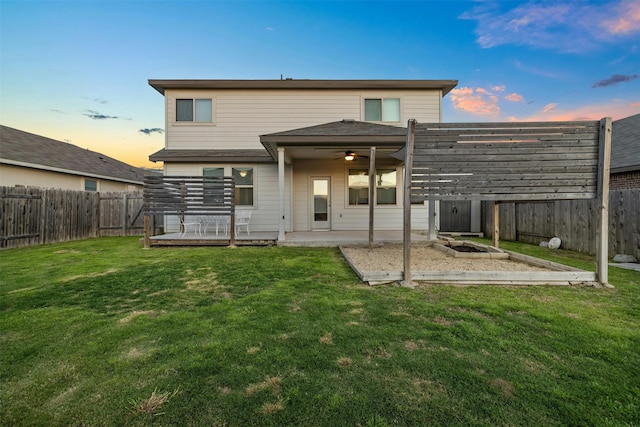 back house at dusk featuring a wooden deck, a yard, and a patio