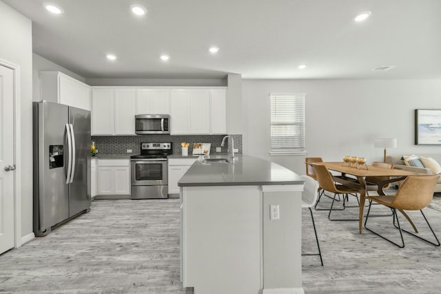 19004 Quebrada Dr, Pflugerville, TX 78660 - kitchen with appliances with stainless steel finishes, a peninsula, light wood finished floors, a breakfast bar area, and white cabinets