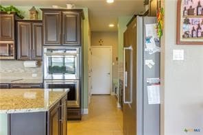 kitchen featuring dark brown cabinetry, backsplash, light stone counters, and appliances with stainless steel finishes