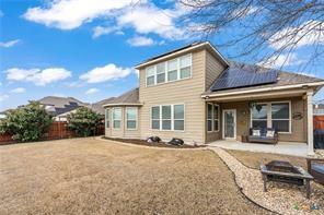 back of house with a yard, a fire pit, a patio, and solar panels