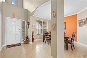 entryway with a high ceiling, ornamental molding, and light tile patterned floors