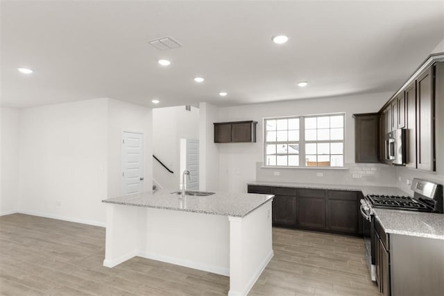 kitchen featuring stainless steel appliances, light stone countertops, a sink, visible vents, and a kitchen island with sink