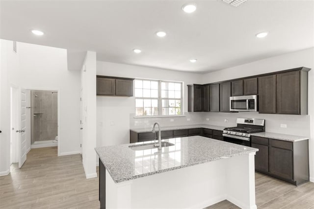 kitchen featuring a sink, stainless steel appliances, an island with sink, and dark brown cabinetry