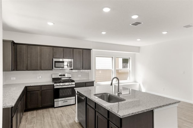 kitchen with a sink, tasteful backsplash, appliances with stainless steel finishes, a kitchen island with sink, and dark brown cabinets