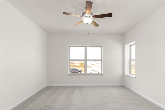 spare room featuring a ceiling fan, baseboards, a healthy amount of sunlight, and light colored carpet