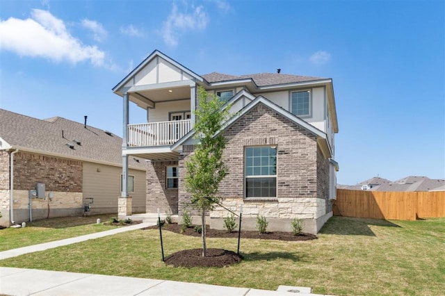 view of front facade with a balcony, brick siding, fence, and a front lawn