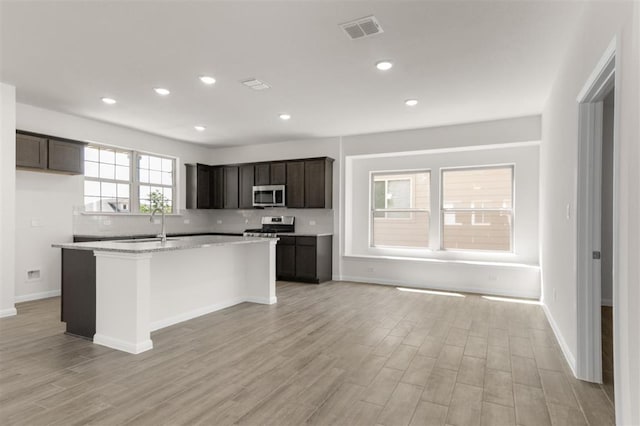 kitchen with tasteful backsplash, appliances with stainless steel finishes, light wood-style flooring, a kitchen island with sink, and visible vents