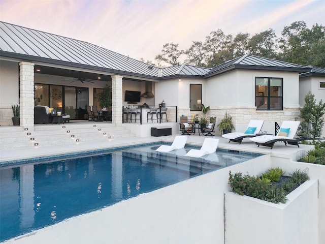 pool at dusk with a patio area, ceiling fan, and a bar