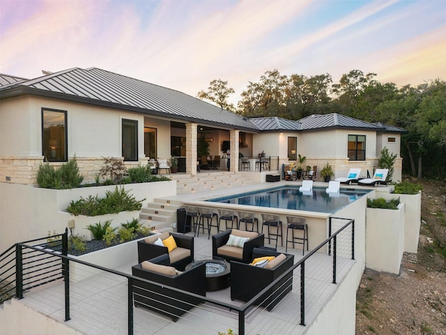 pool at dusk featuring an outdoor living space with a fire pit and a patio area