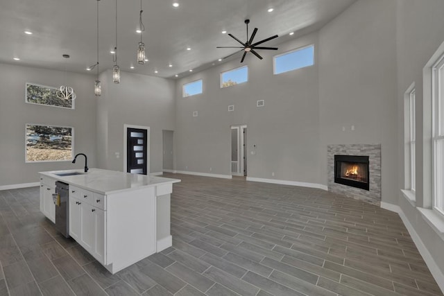 kitchen featuring sink, a kitchen island with sink, hanging light fixtures, white cabinetry, and a fireplace