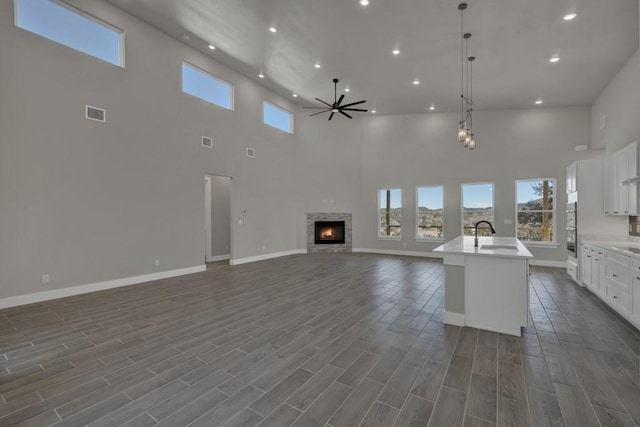 kitchen with ceiling fan, a fireplace, white cabinets, a center island with sink, and decorative light fixtures