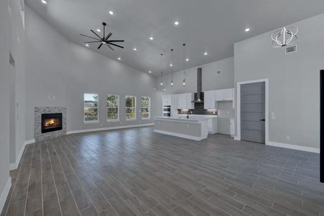 unfurnished living room featuring sink, dark hardwood / wood-style flooring, a towering ceiling, ceiling fan, and a fireplace