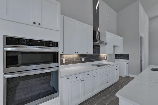 kitchen with wall chimney range hood, double oven, decorative backsplash, and white cabinets