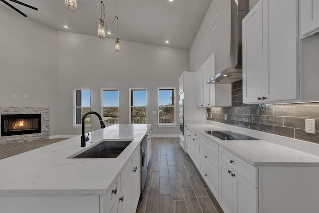 kitchen featuring pendant lighting, sink, a kitchen island with sink, light stone counters, and wall chimney exhaust hood