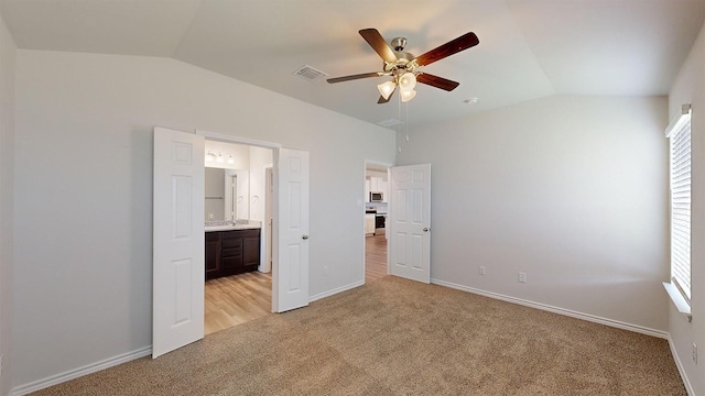 unfurnished bedroom with connected bathroom, vaulted ceiling, light colored carpet, and ceiling fan