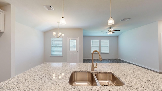 kitchen with lofted ceiling, sink, hanging light fixtures, light stone counters, and ceiling fan with notable chandelier