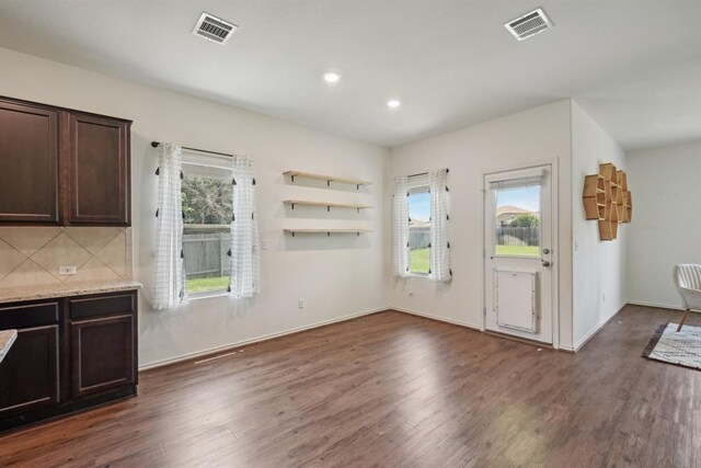 kitchen with dark hardwood / wood-style floors, light stone countertops, dark brown cabinets, and backsplash