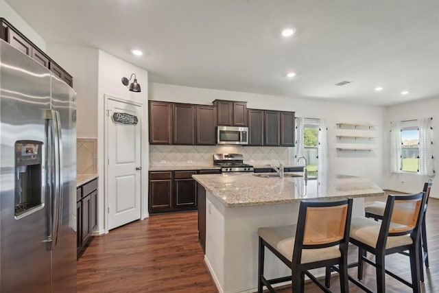 kitchen featuring a breakfast bar, dark hardwood / wood-style flooring, light stone counters, stainless steel appliances, and a center island with sink